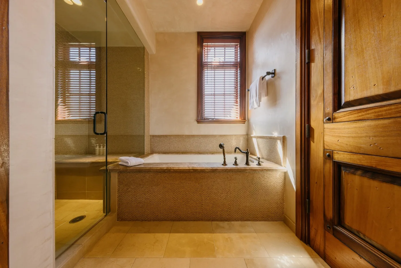 A bathroom with a bathtub, a glass shower, and a window with blinds.