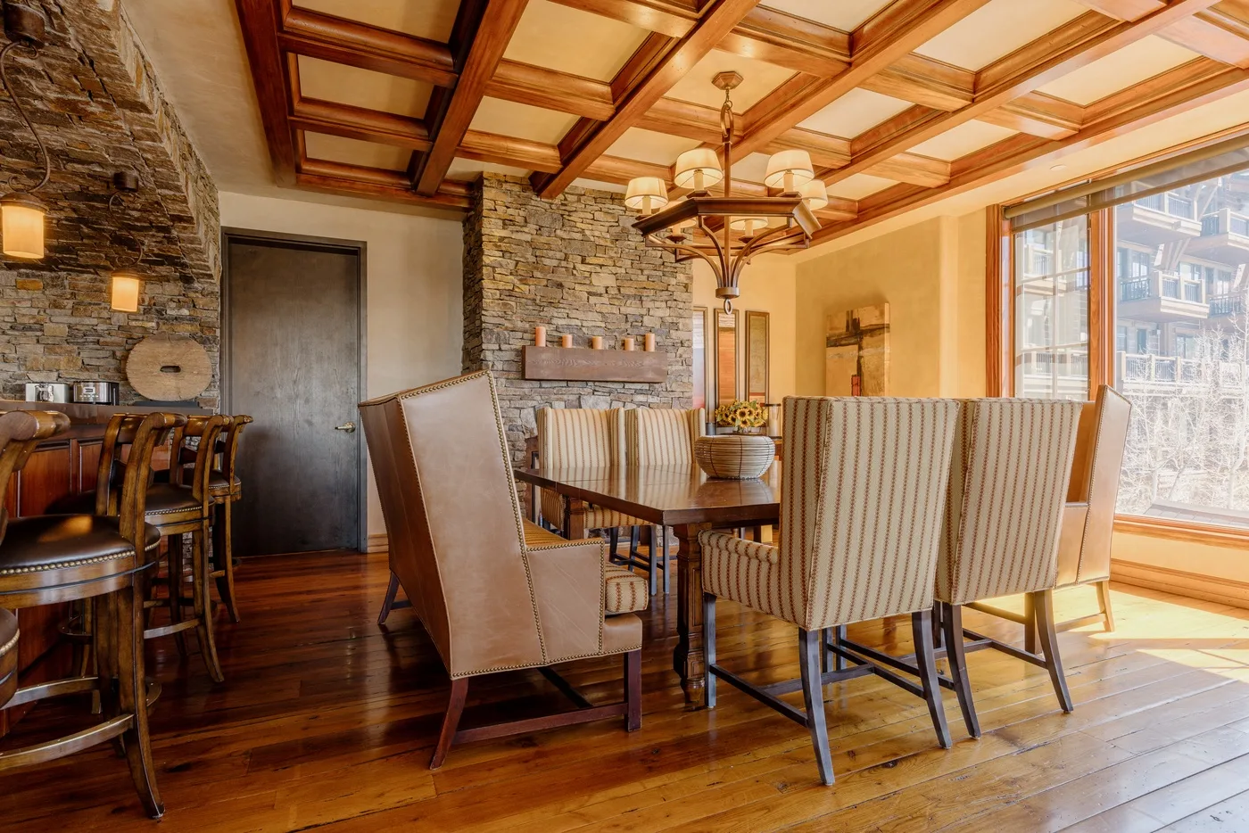 A dining room with a long table, upholstered seating, and large windows.
