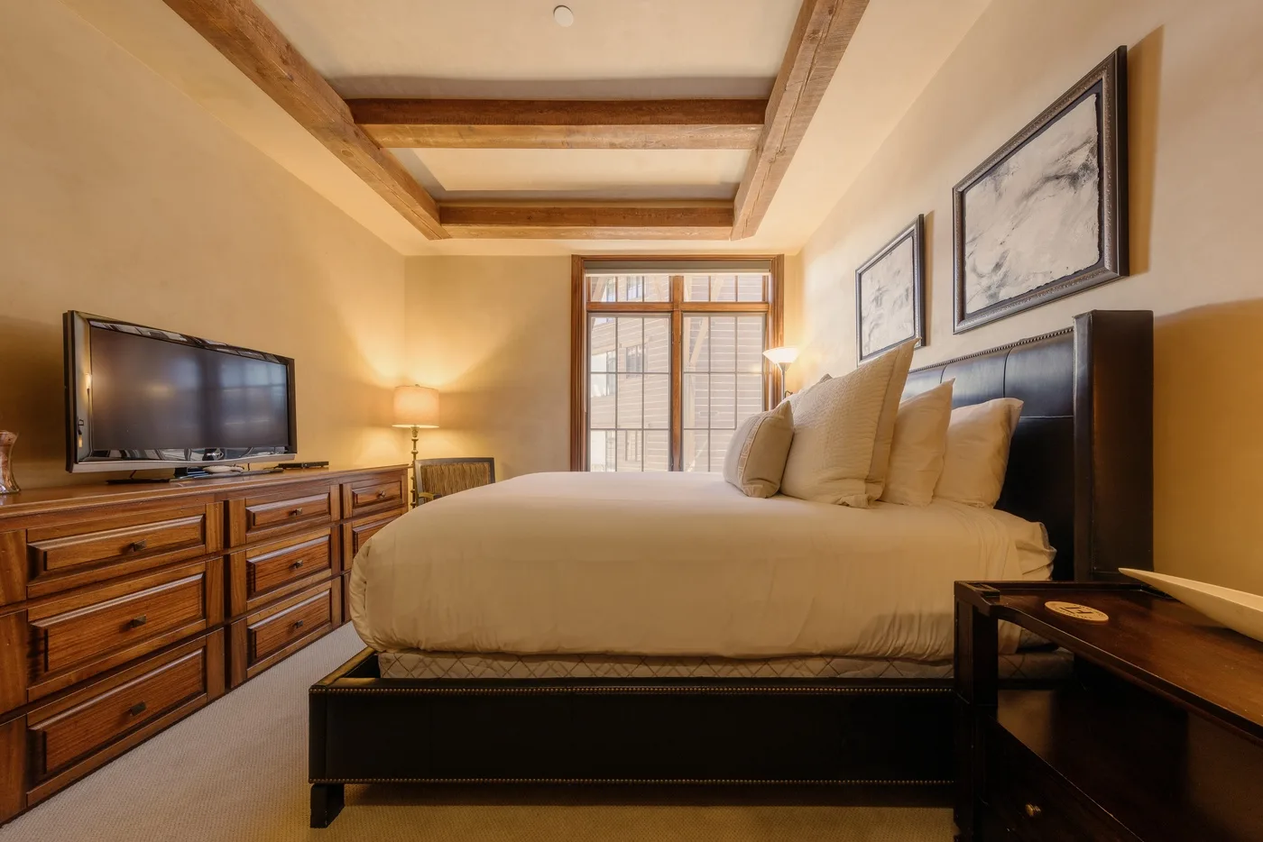 A bedroom with a large bed, wooden dressers, and framed artwork.