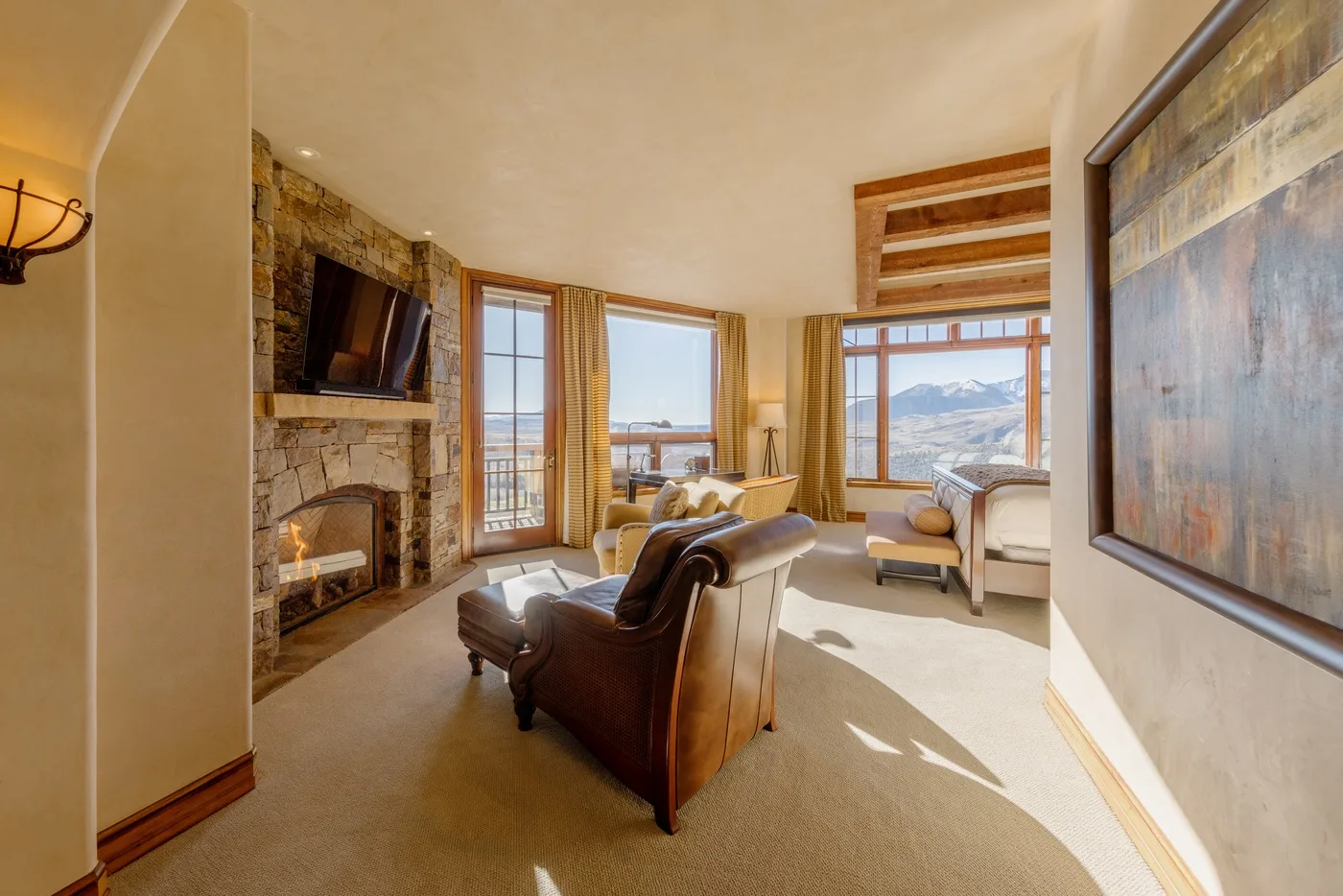 A living room with seating, a stone fireplace, and large windows overlooking the landscape.
