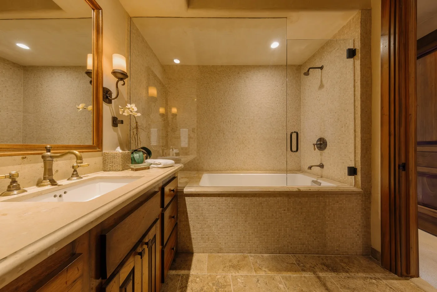 A bathroom with a long vanity and a glass-enclosed bathtub.
