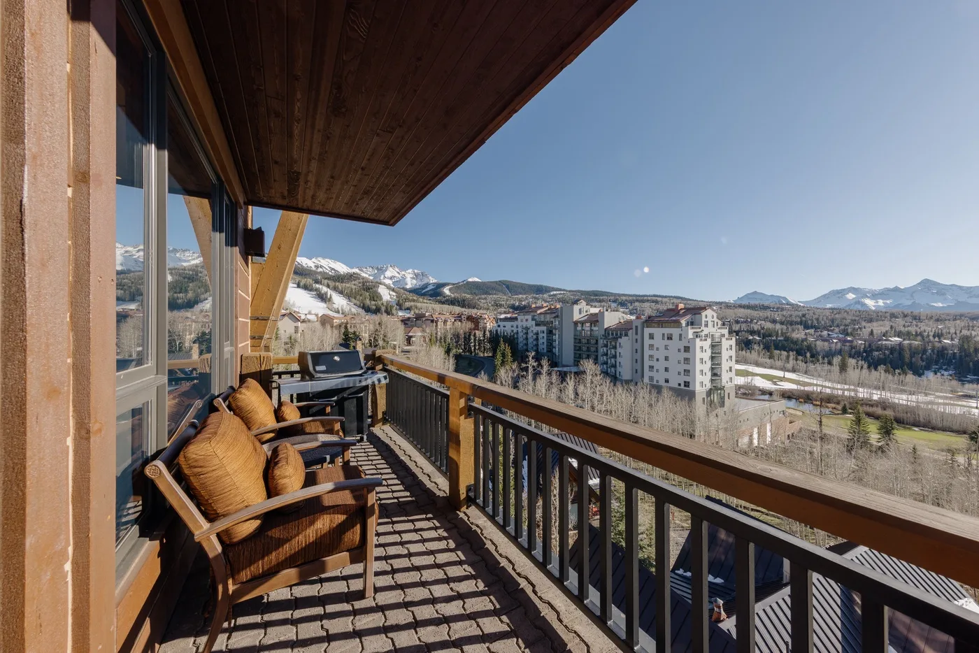 A balcony with seating overlooks a mountain landscape and nearby buildings.