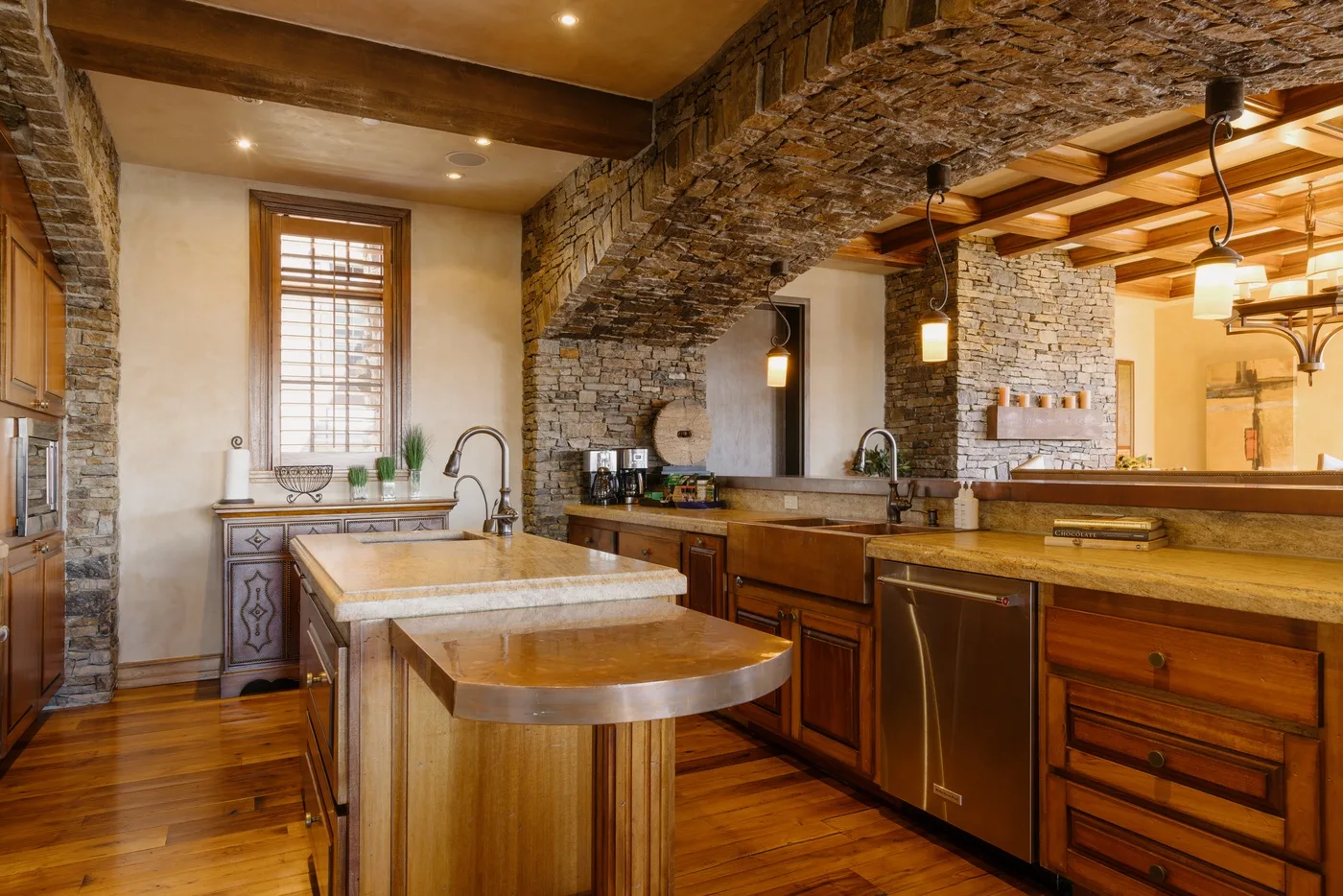 A spacious kitchen with a central island, wooden cabinetry, and a stone arch.