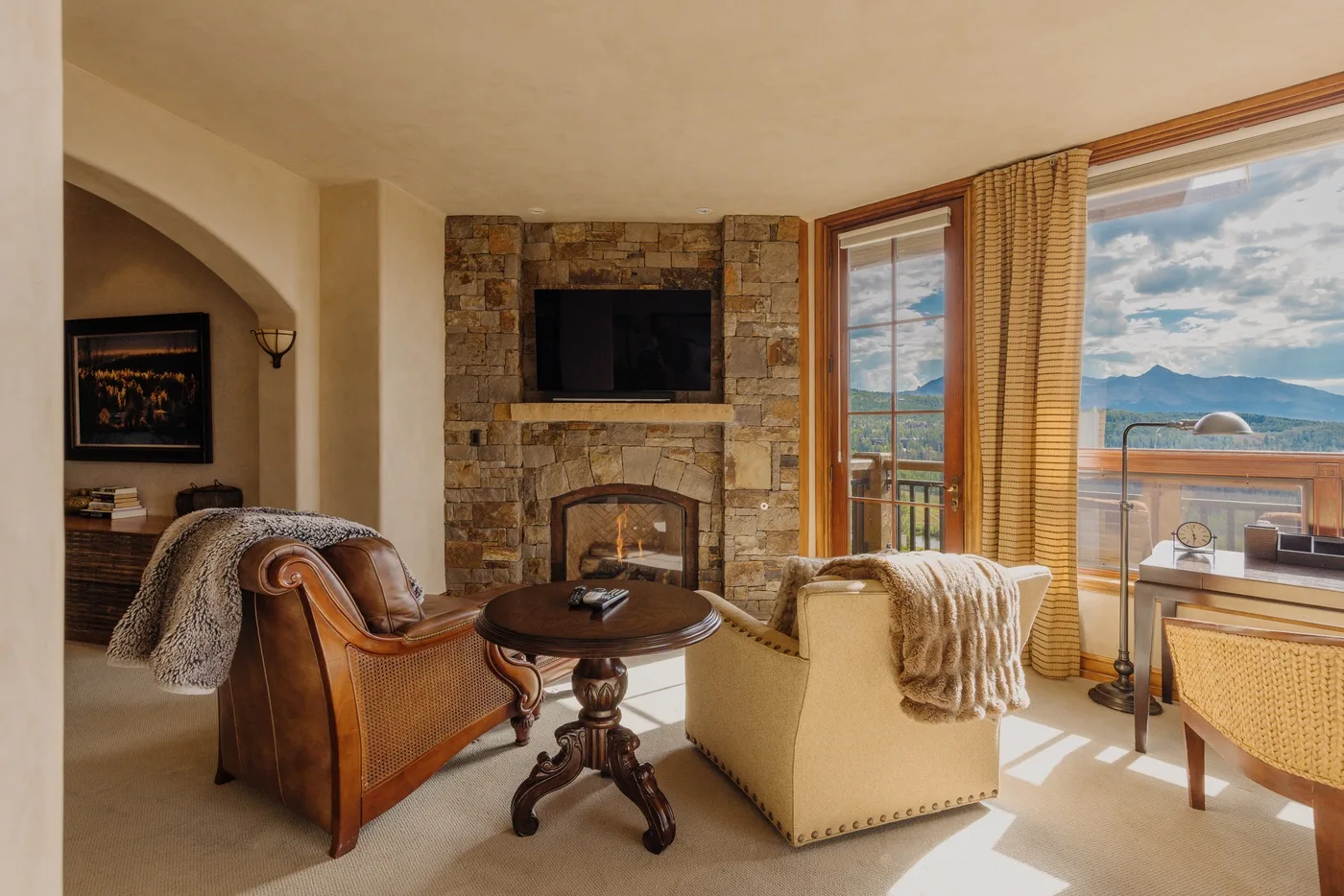 Sala de estar con chimenea de piedra, asientos y grandes ventanas con vistas a las montañas.