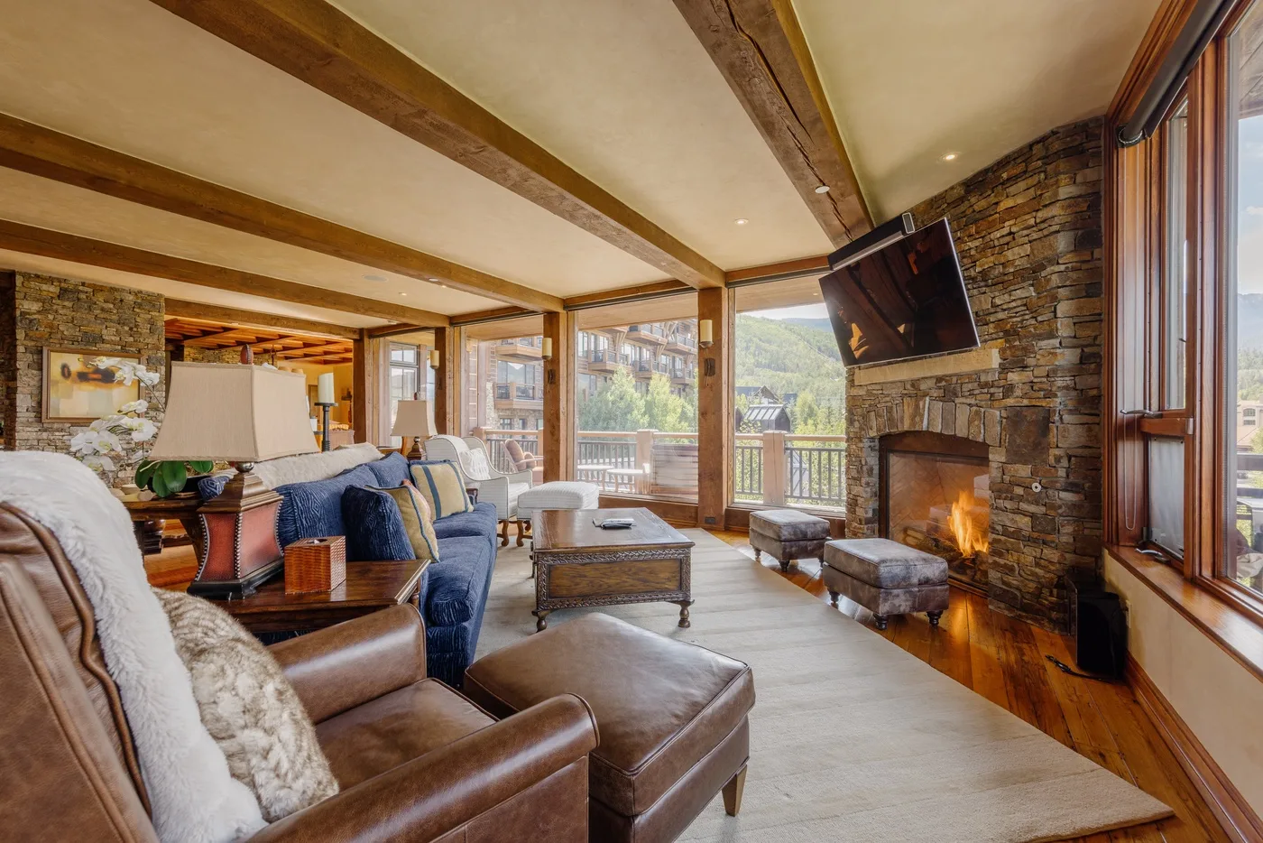 A living room with seating, a stone fireplace, and windows overlooking the mountains.