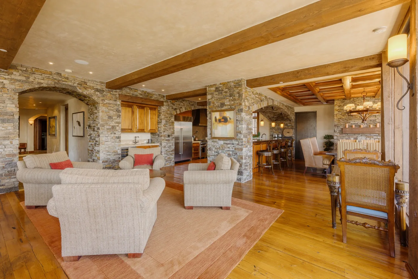 Open-plan living and dining area with seating, a kitchen, and exposed wooden beams.