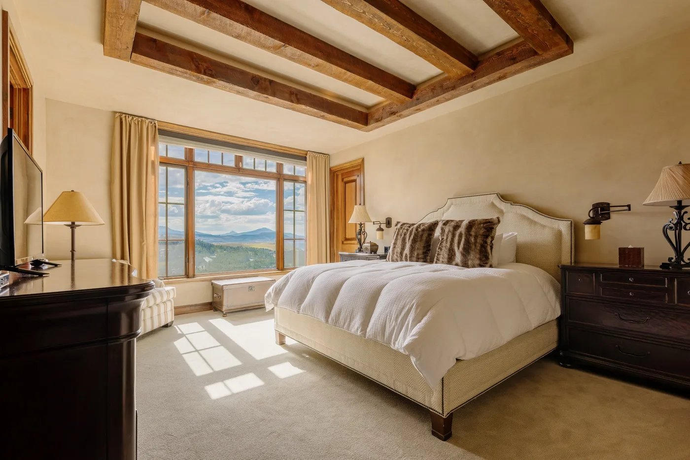 A bedroom with a large bed, dark bedside furniture, and a wide window.