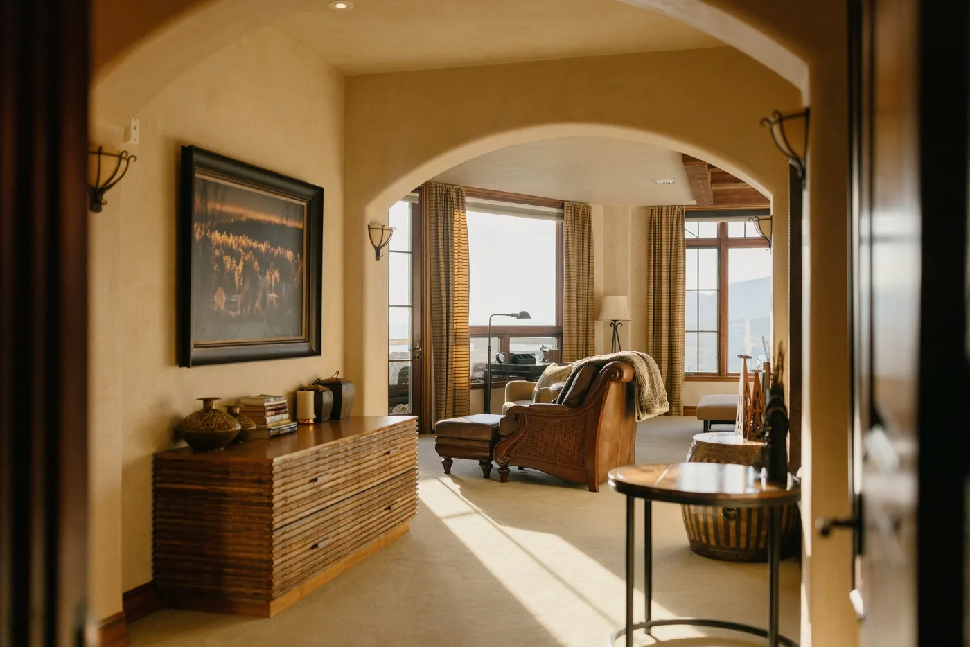 A warm living room with seating and large windows overlooking the water.