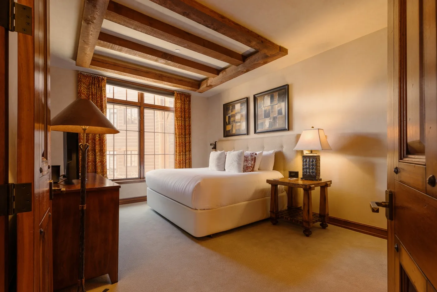 A bedroom with a neatly made bed, framed pictures, and a large window.