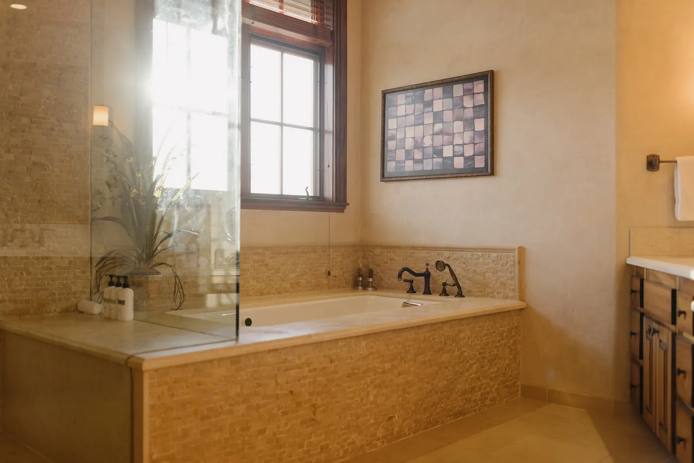 A bathroom with a built-in bathtub beneath a window and framed wall art.