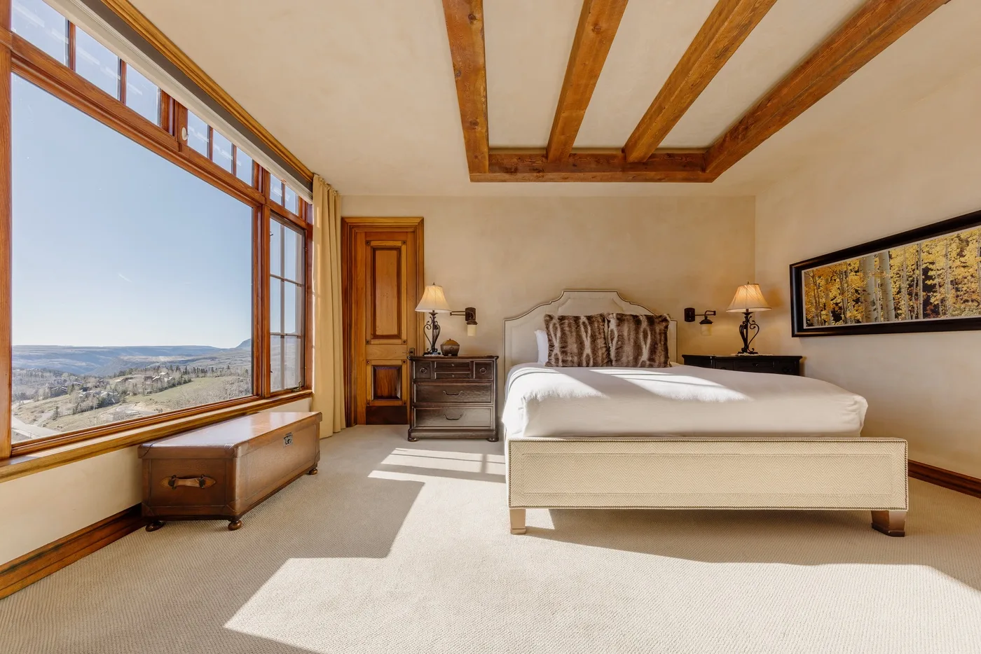 A bedroom with a bed, wooden ceiling beams, and a large window overlooking the landscape.