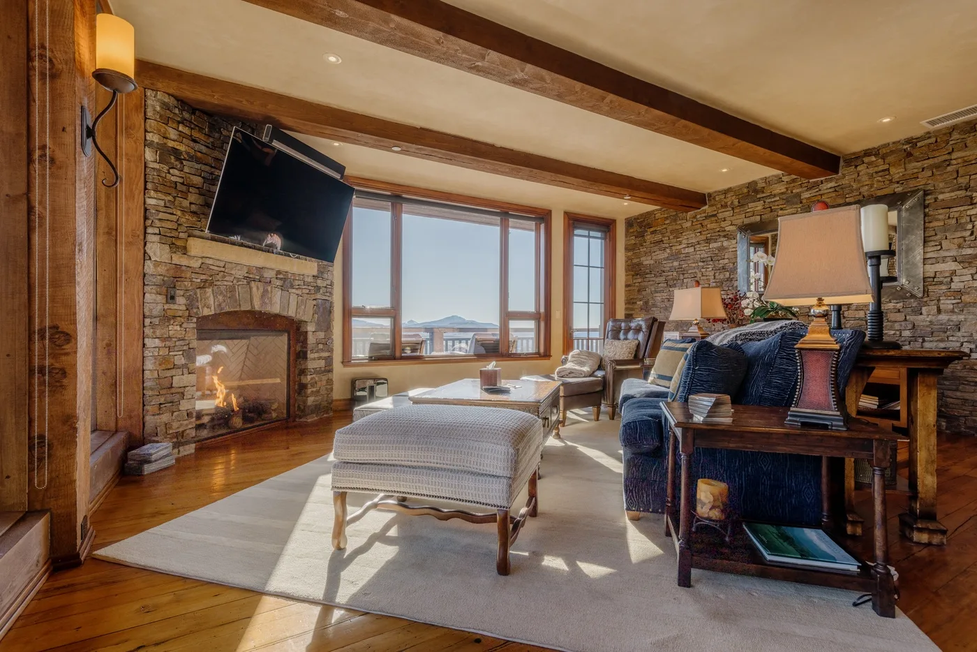 A living room with a stone fireplace, seating, and large windows.