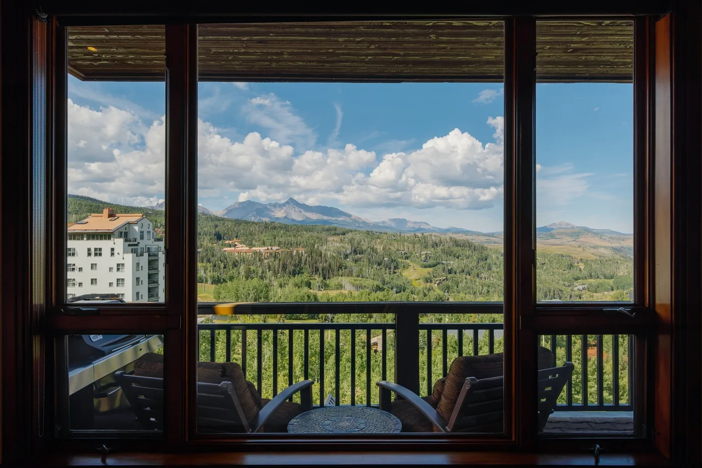 Un balcón con asientos ofrece vistas a un valle verde y montañas lejanas.