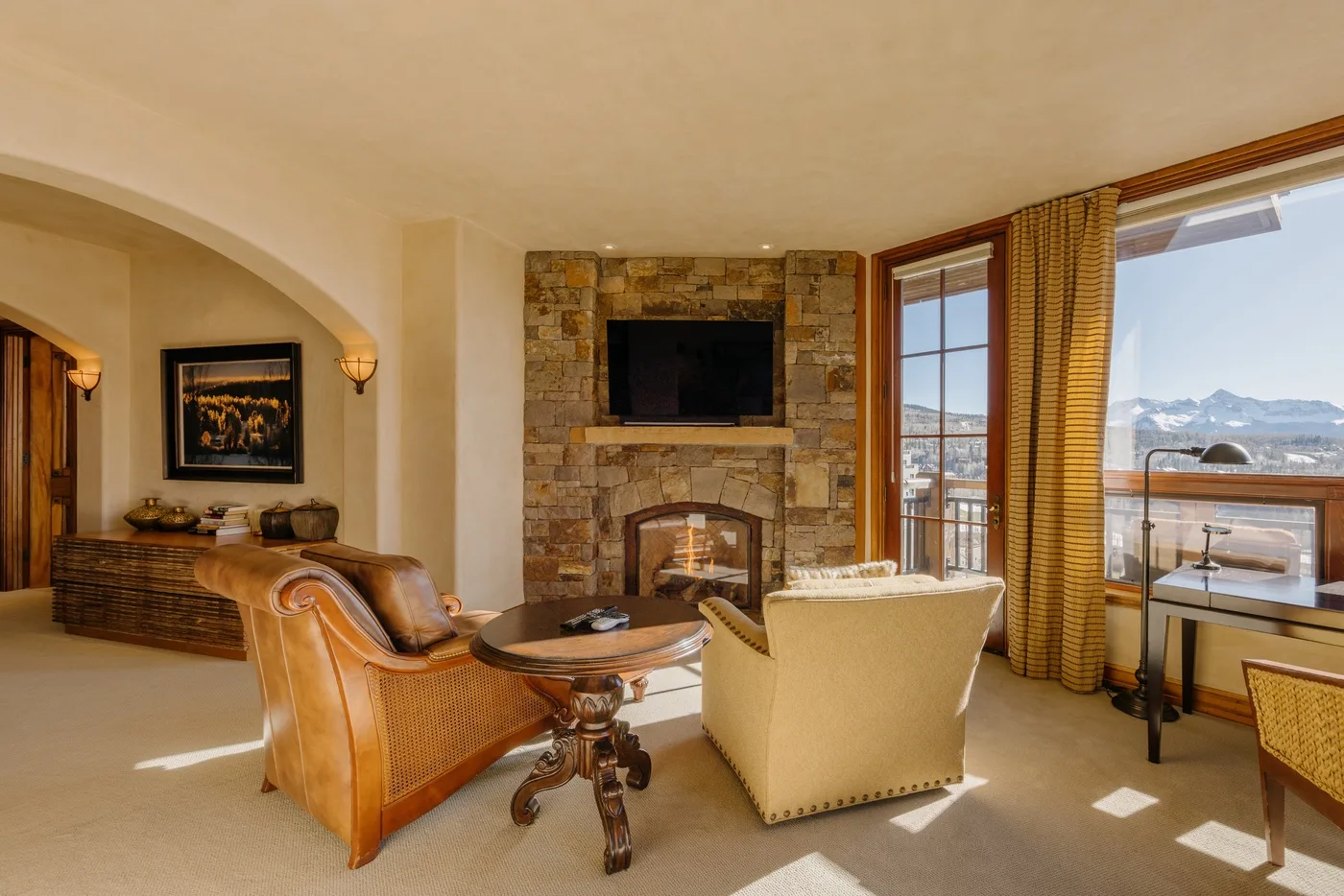 Una sala de estar con asientos, una chimenea de piedra y grandes ventanas con vistas a las montañas.