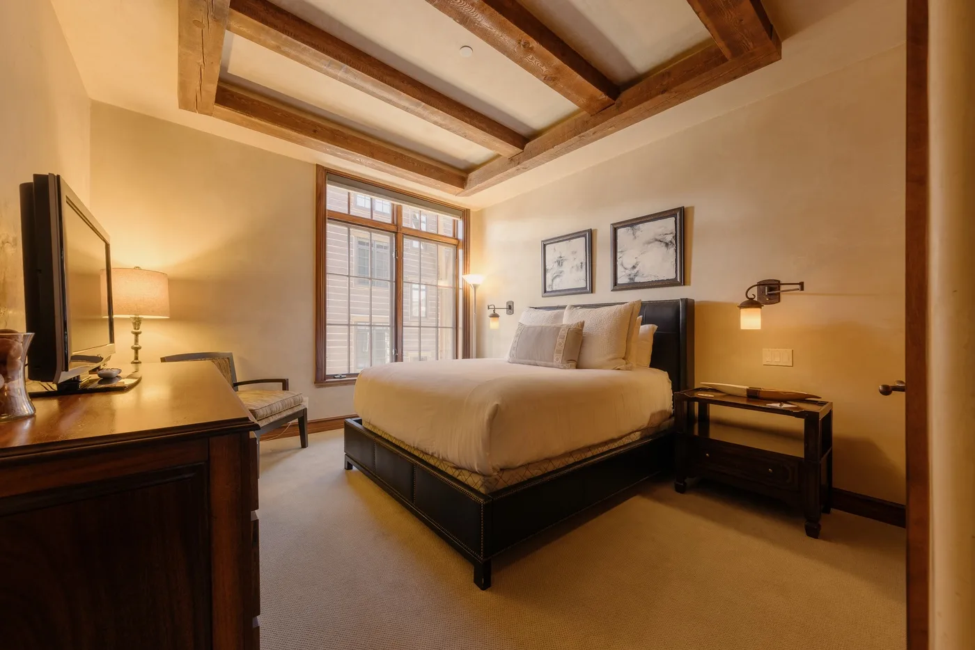 A bedroom with a large bed beneath exposed wooden ceiling beams.