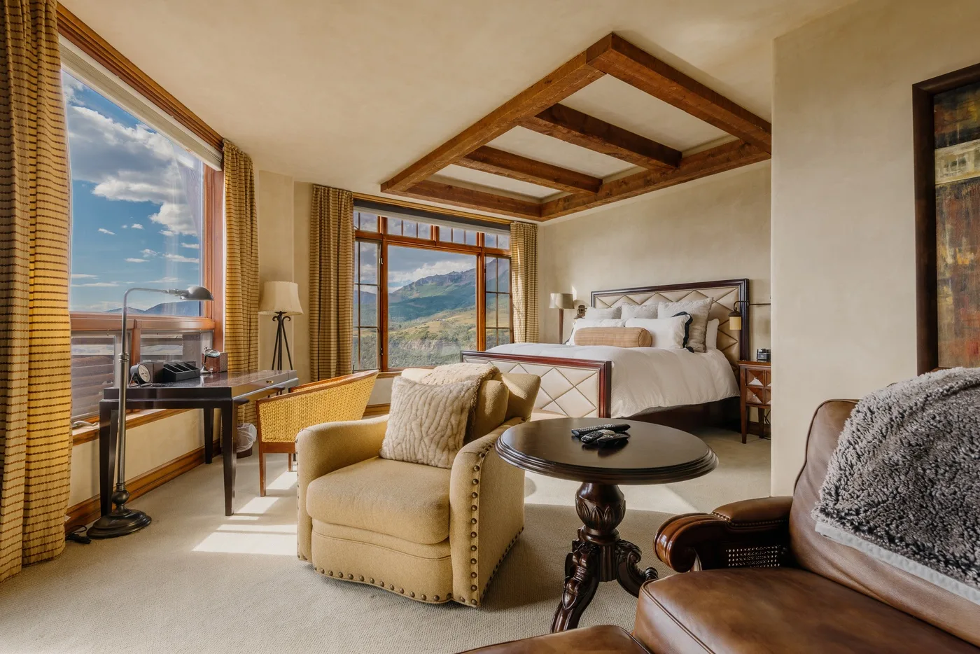 A bedroom with a bed and seating beside large windows overlooking a mountain landscape.