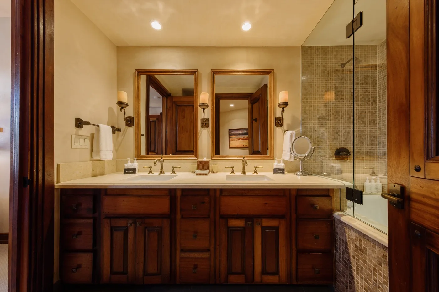 A bathroom vanity with twin sinks sits beside a glass-enclosed shower.