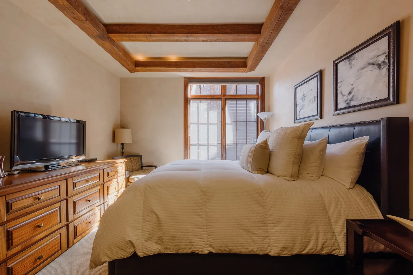A bedroom with a large bed, wooden dresser, and television.