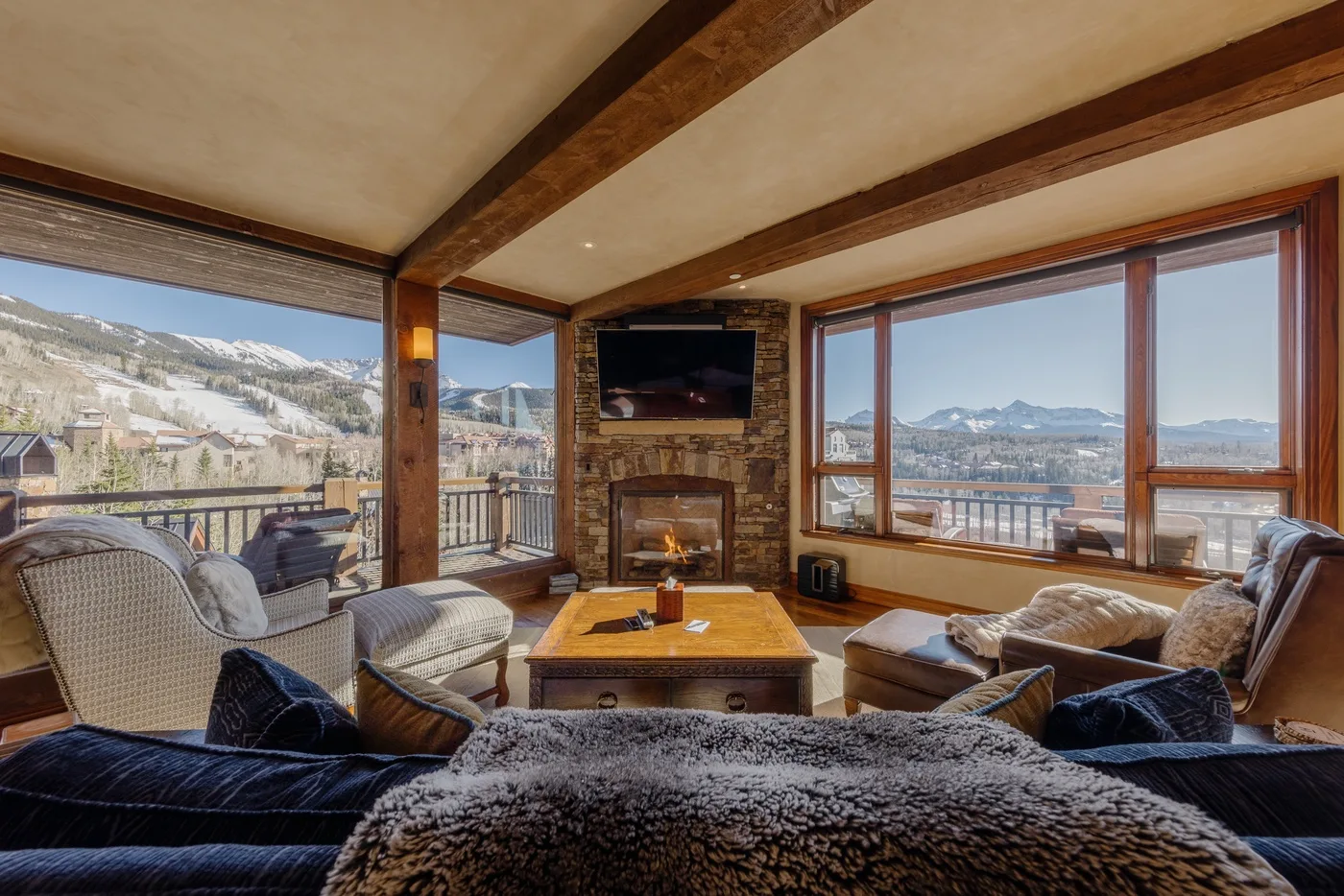 Una sala de estar con asientos alrededor de una mesa de centro y grandes ventanas con vistas a las montañas.