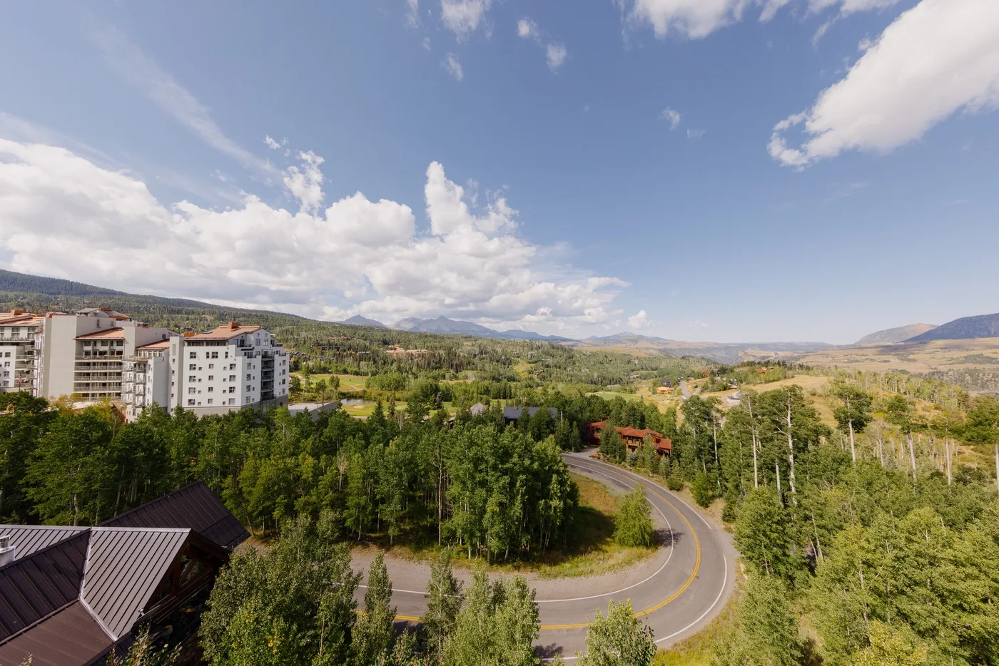 A winding road curves through a green landscape beneath a broad, cloudy sky.