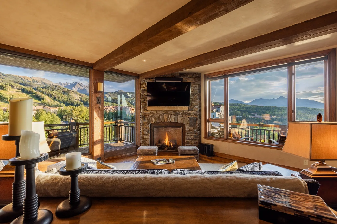Una sala de estar con chimenea de piedra y amplias ventanas con vistas a un paisaje montañoso.