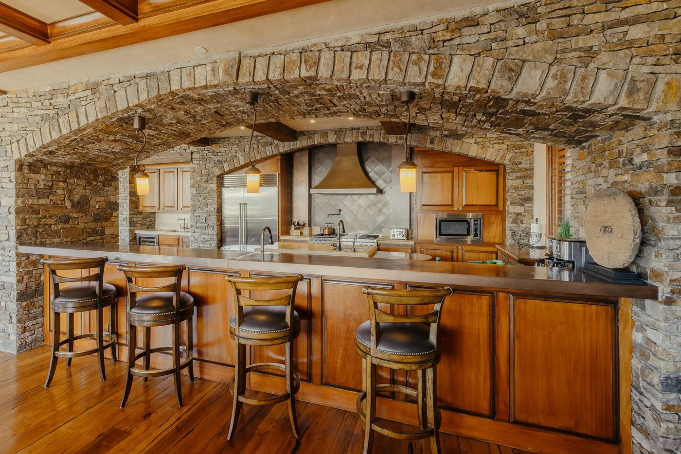 Una cocina con una larga isla de madera y asientos bajo un arco de piedra.