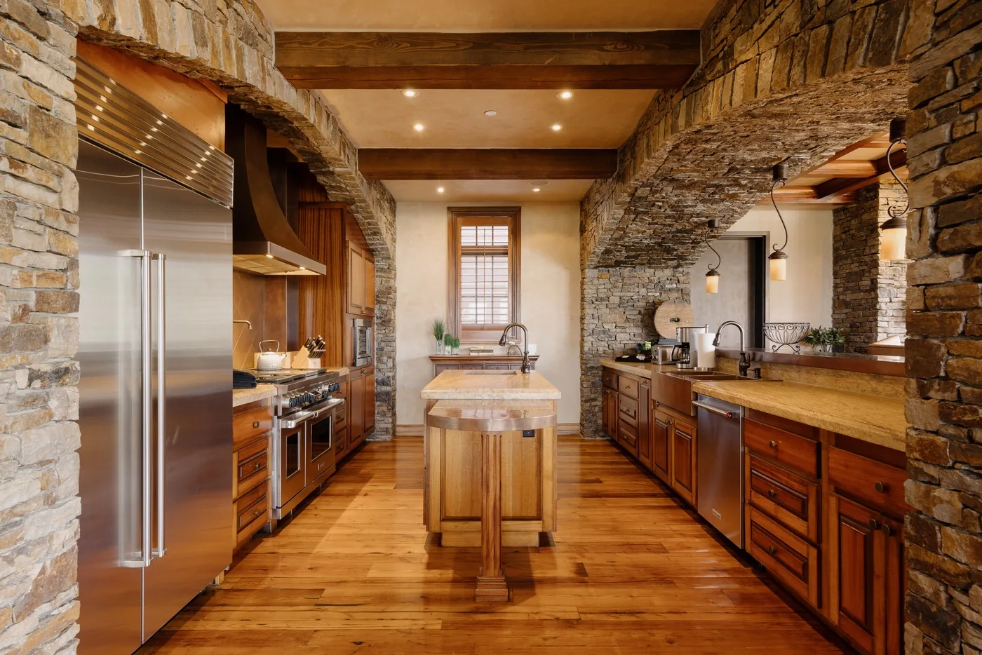 Una cocina rústica con una isla central, gabinetes de madera y paredes de piedra.