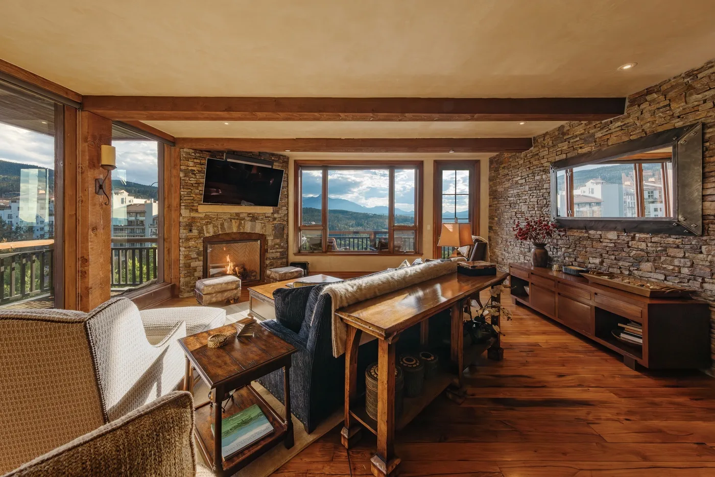 Una sala de estar con asientos, una mesa de madera y grandes ventanas con vistas a las montañas.