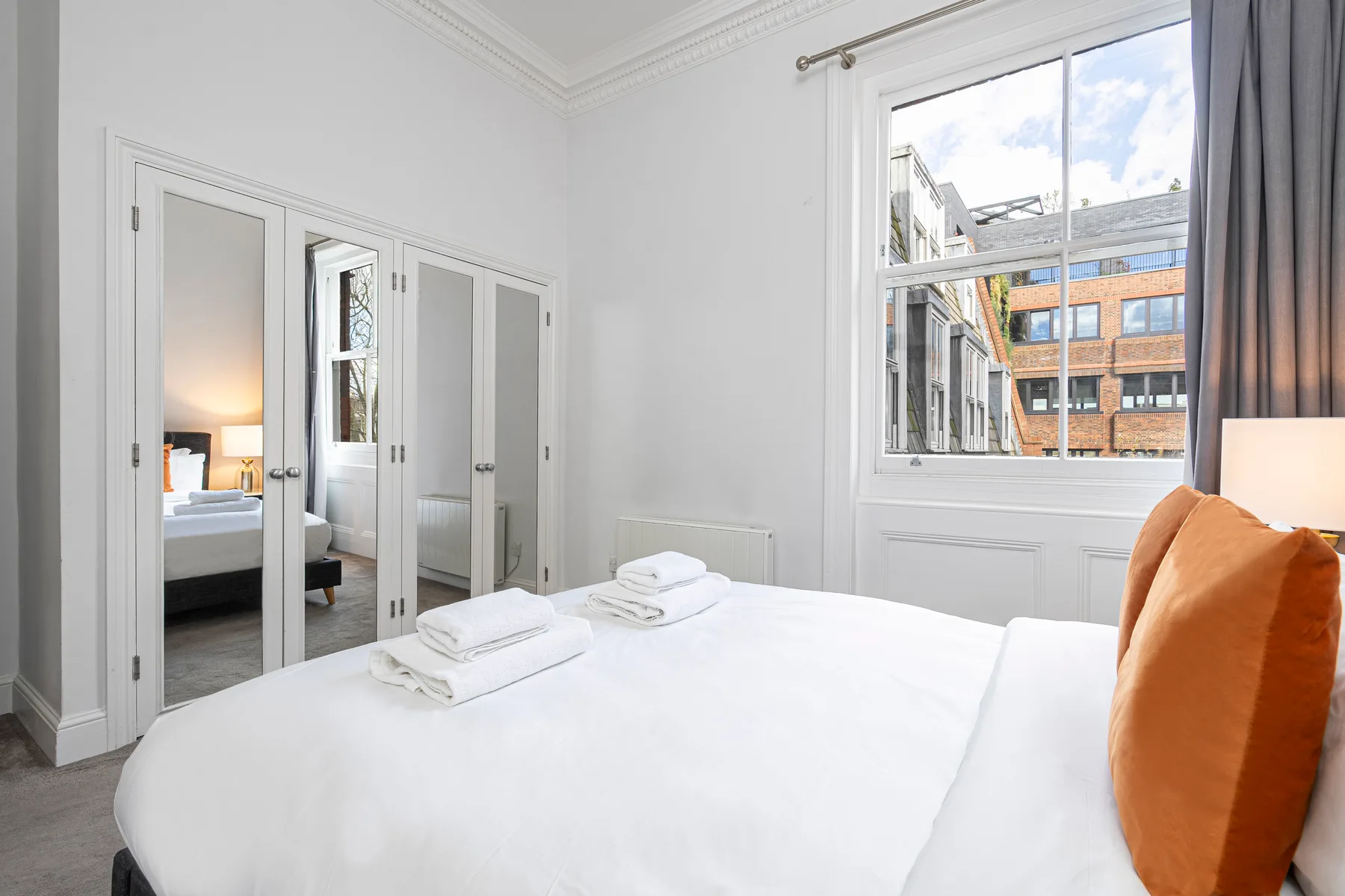 Un dormitorio luminoso con una cama blanca, toallas dobladas y una ventana grande.