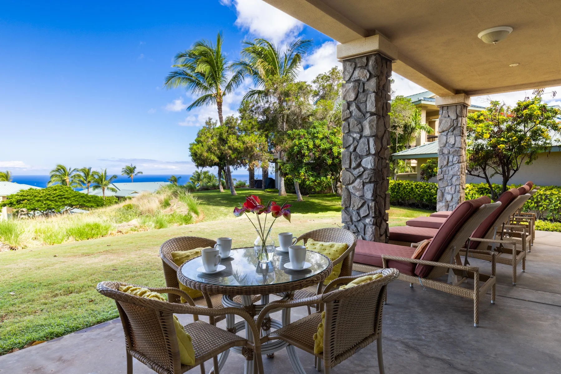 An outdoor dining patio overlooks a landscaped lawn and the ocean.