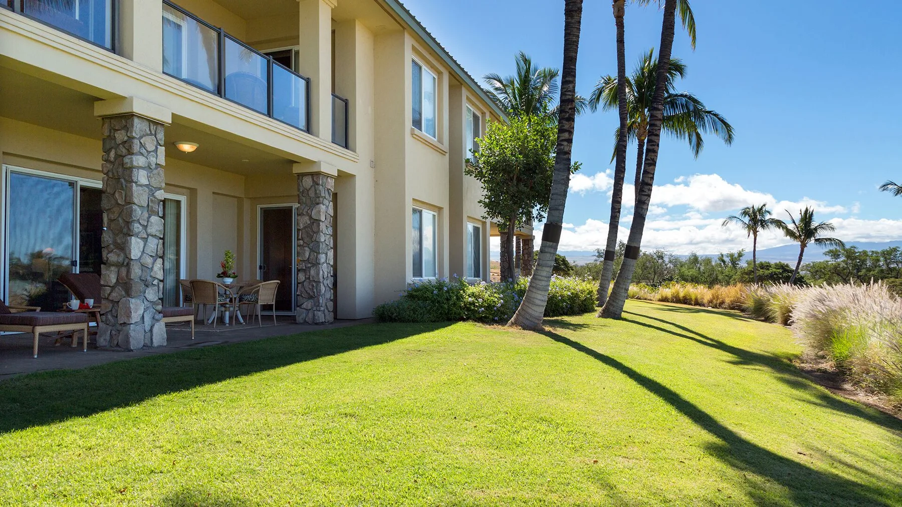 A landscaped lawn beside a two-story building, with palm trees and coastal views.
