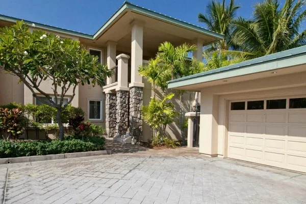 A house exterior with a paved driveway, garage, and tropical landscaping.