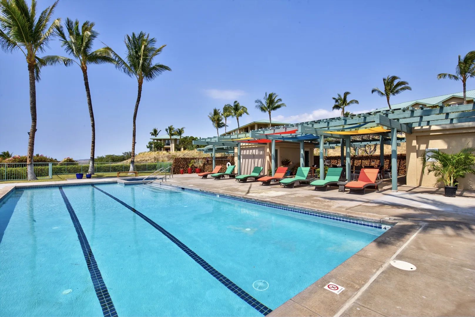 A swimming pool beside a shaded outdoor seating area and palm trees.