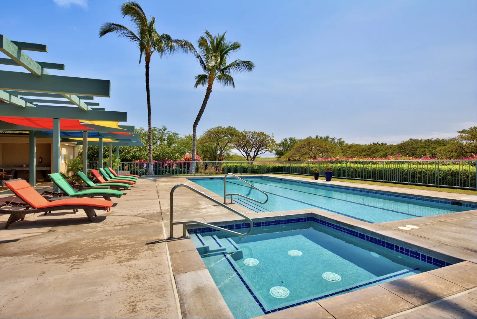 An outdoor swimming pool with a shallow section, palm trees, and lounge seating.