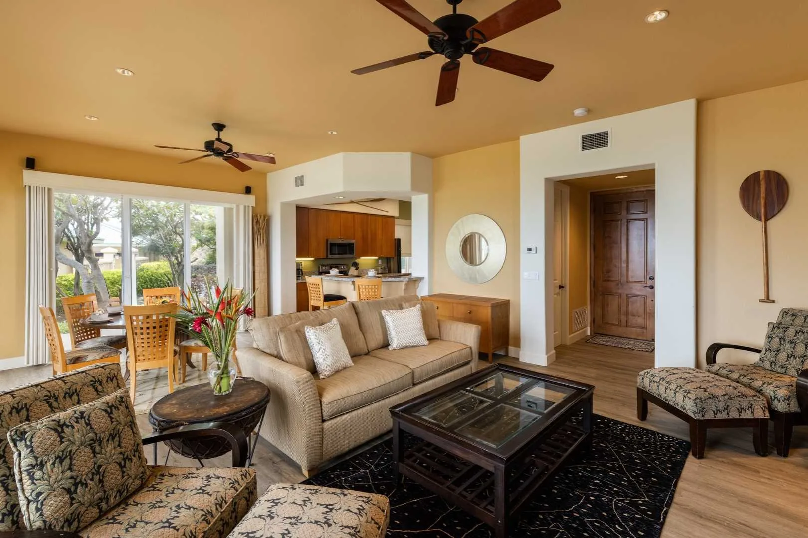 A living room with beige seating, a glass coffee table, and large windows.