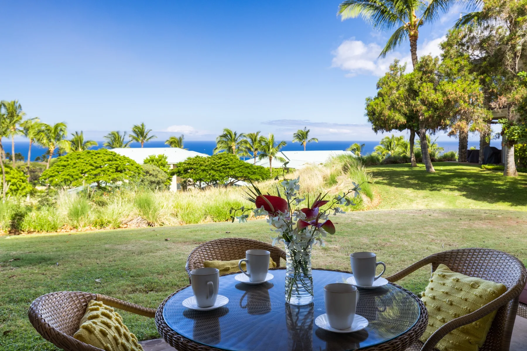 An outdoor seating area overlooks a grassy garden and the ocean.