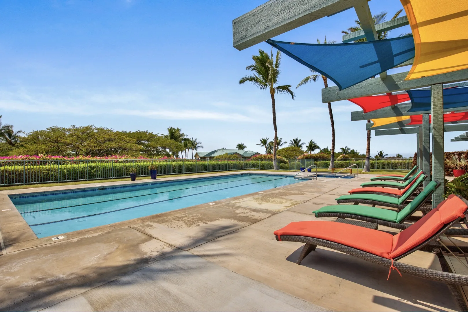 An outdoor swimming pool with lounge chairs beneath colorful shade canopies.