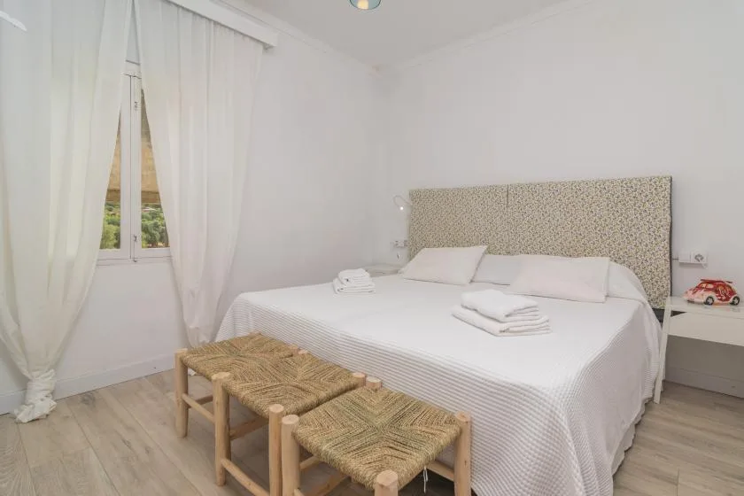 A bright bedroom with a neatly made bed and woven benches at its foot.