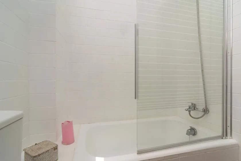 A tiled bathroom with a bathtub and glass shower screen.