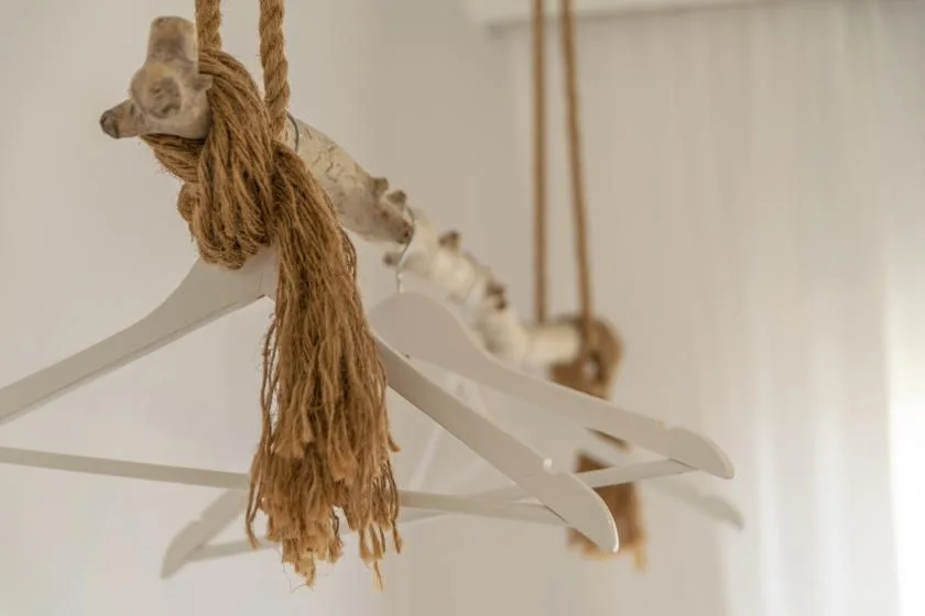 A close-up of white hangers suspended from thick rope against a light wall.