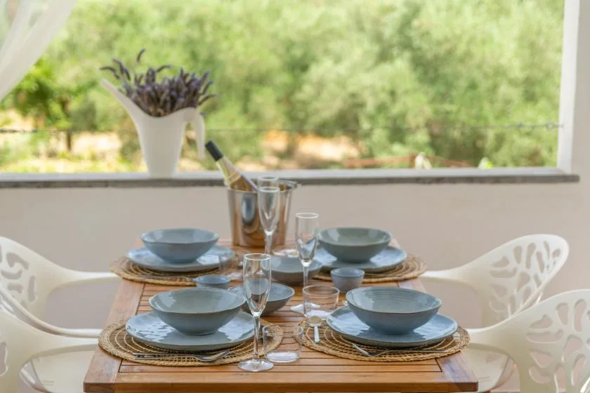 A dining table is set with blue dishes beside a large open window.