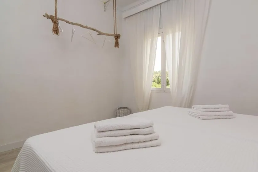 A bedroom with a neatly made bed and folded towels beside a curtained window.