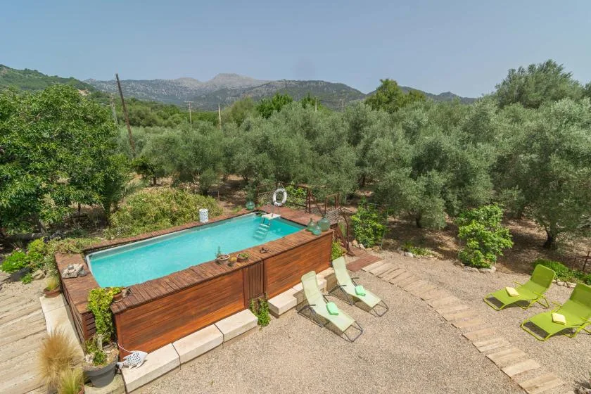 An outdoor swimming pool sits beside a gravel patio with lounge chairs and trees.