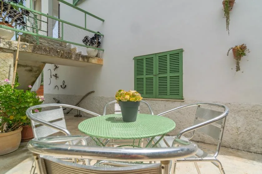 A small courtyard with a green table and metal seating beside a white wall.