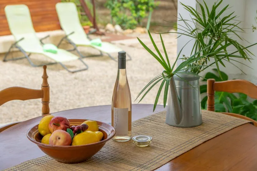 A dining table holds a bowl of fruit and a bottle beside a potted plant.