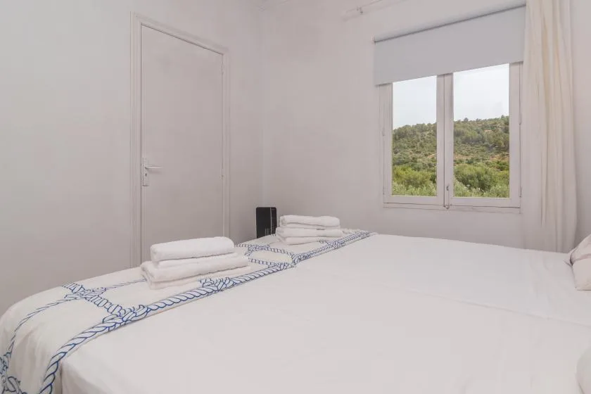 A bright bedroom with white bedding and a window overlooking green hills.