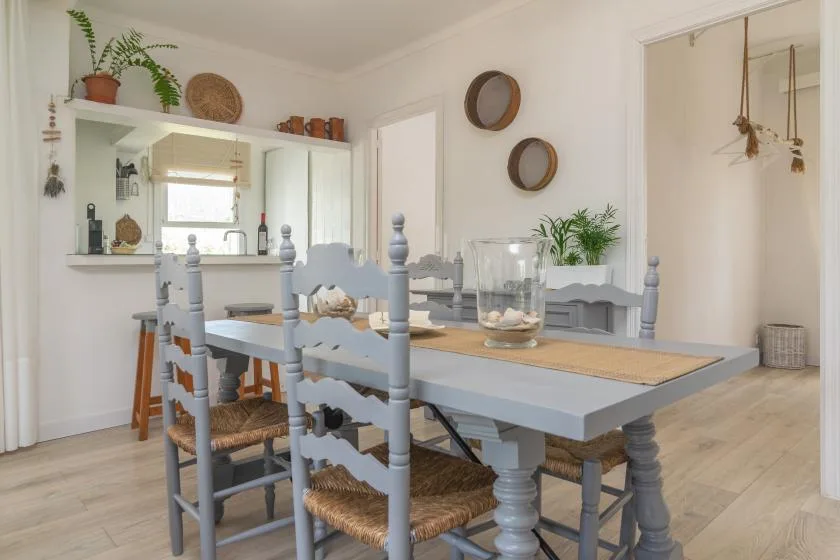 A dining room with a long table, light blue seating, and plants.