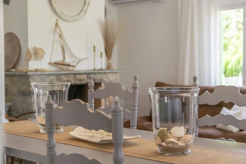 A dining table is set with glass candle holders in front of a fireplace.