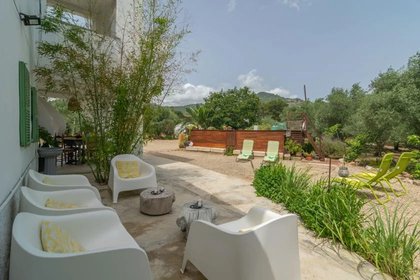 A patio with white seating overlooks a garden and an outdoor pool.