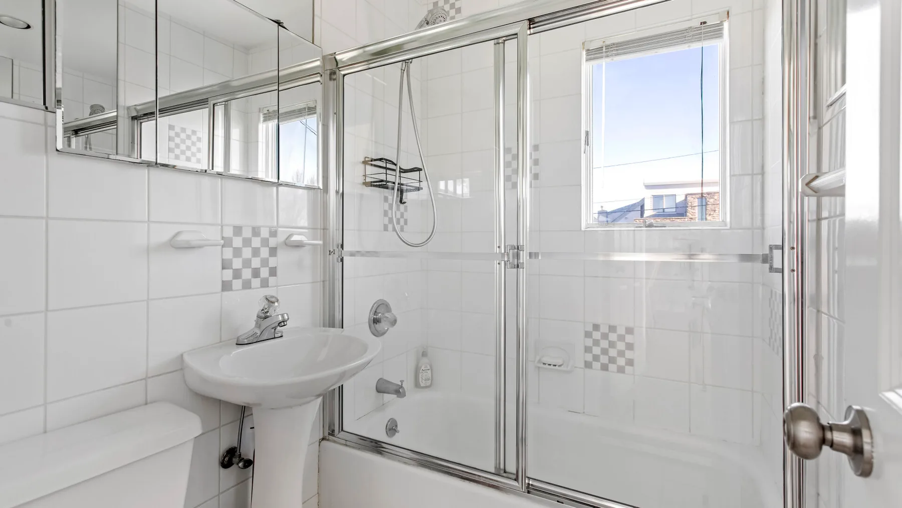 A bright tiled bathroom with a glass shower and pedestal sink.